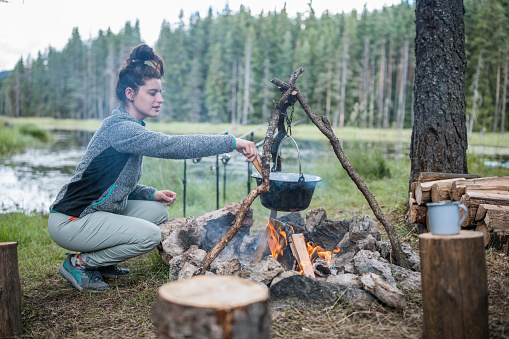 Young woman on camping cooking meal over the campfire.