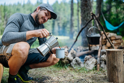 Happy mid adult man on camping having freshly brewed coffee in the morning.
