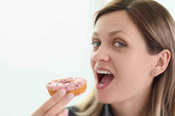 istock Woman bites delicious donut with glaze looking in camera 1644005475