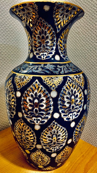 A picture of an oriental style designed vase of blue colour with golden and white details