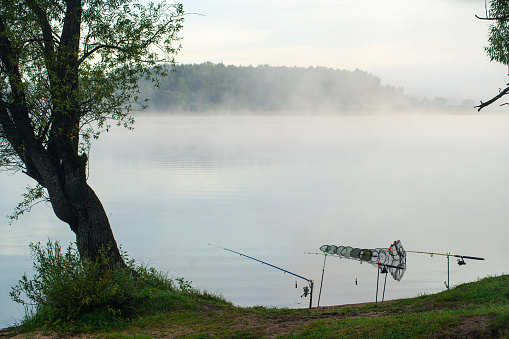 Fishing rods and fishing cage at the river edge in the foggy morning