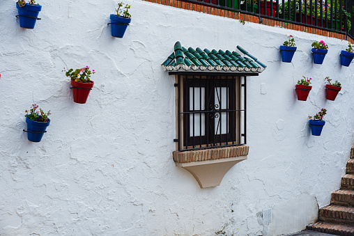 typical façade of a village in Andalusia, Spain, white lime with colored flowerpots, space of