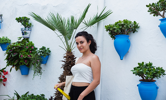 A young woman in black pants and white T-shirt poses next to blue flower pots hanging on a white wall, copying the space.