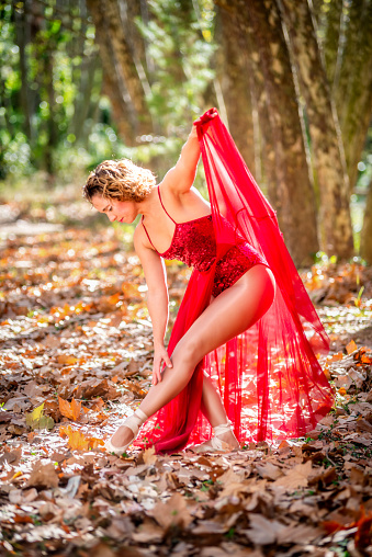 Ballerina ballet woman stretching posing exercising at nature park with red dress