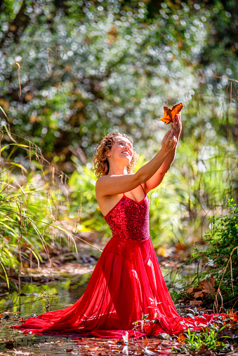 woman in red dress posing with a leaf in the hand at the river in autumn