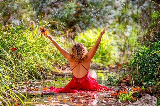 woman in red dress posing with a leaf in the hand at the river in autumn. Splashing water