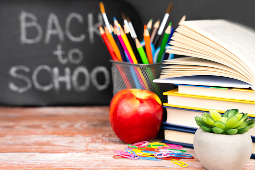 Blurred background with blackboard, books, an apple and bright school supplies. The concept of education. Copy space. Selective focus.
