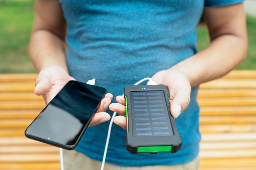 Man charging smartphone with solar panel in a city in a sunny summer day.
