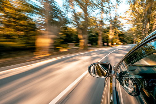 In the autumn, a car drives along the country road, creating a mesmerizing motion blur effect. As it speeds ahead, the surrounding environment becomes a blur of colors and shapes. Trees pass by in a rural landscape, accentuating the sense of a long journey. This exhilarating travel experience captures the thrill of speed and the allure of the open road. Hungary