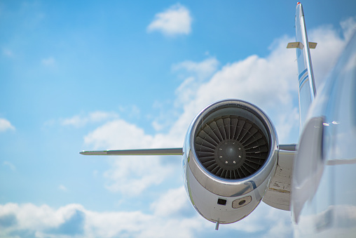 The jet engine of a small private jet.  The focus is on the engine fan and cowling.  A blue sky filled with clouds is in the background.  Selective focus is used.