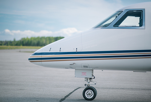 The nose of a small private jet parked on the apron at a small regional airport in Canada.  The landing gear and front windows can be seen.