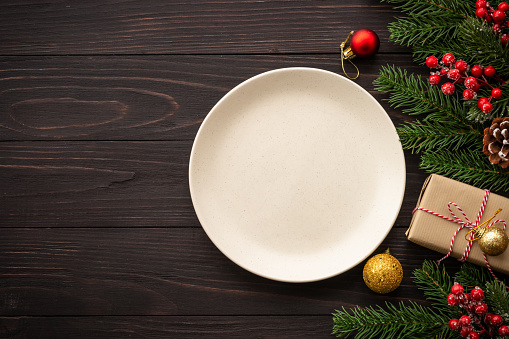 Christmas food, christmas table holiday dinner with craft plate and christmas decorations on dark wooden background. Top view with copy space.