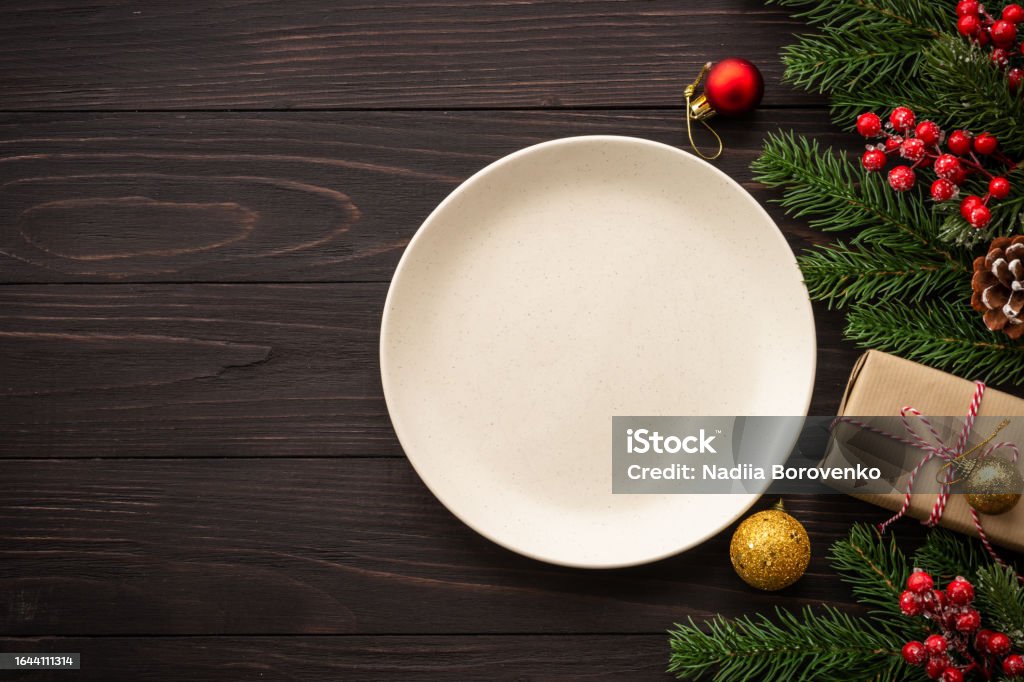 Christmas table setting with plate, cutlery and christmas decorations on white background. Christmas food, christmas table holiday dinner with craft plate and christmas decorations on dark wooden background. Top view with copy space. Christmas Stock Photo