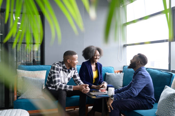 Enthusiastic professionals discussing plans for new business Business people in 20s and 30s sitting together on sofa in Nairobi coworking office, drinking coffee, and sharing ideas for development. kenyan man stock pictures, royalty-free photos & images
