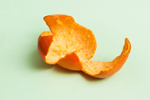 Skin of a mandarin orange, skilfully removed from the fruit in a single piece, lying discarded on a mint green background.