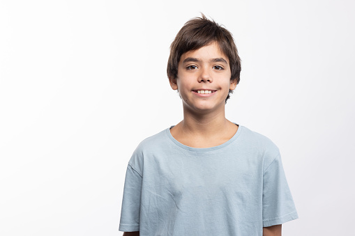 Happy cute little boy of African ethnicity in white t-shirt standing in front of camera against blue background in isolation