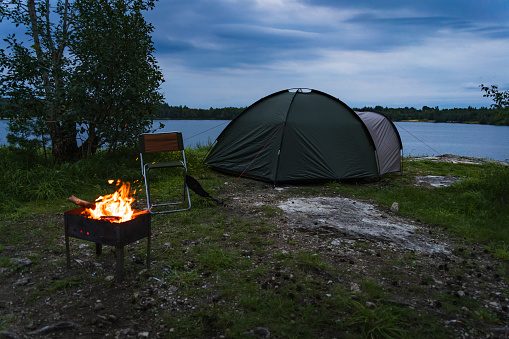 Wild camping in nature in Estonia. A tent set on the shore of a rummu quarry, a brazier with a fire. Photo at dusk. High quality photo