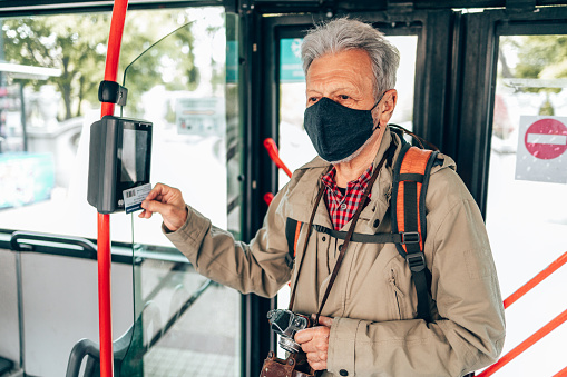Handsome senior tourist using public transport bus. He is wearing protective face mask against virus pandemic infection.