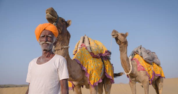 istock Indian man posing with camels on sand dunes, Rajasthan, India 1644162401