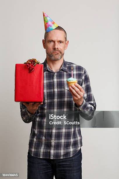 Hombre Decepcionado En Fiesta Hat Holding Magdalenas Con Glaseado Y Presente Foto de stock y más banco de imágenes de Gorro de fiesta