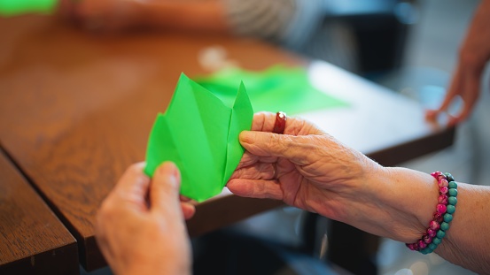A close-up photo of a senior woman learning making origami as for physiotherapy activity in nursing home.