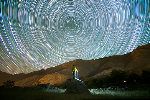 rear view of man climbed on a rock looking at star trails at night. High quality photo