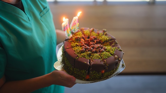 An unrecognizable female nurse is carrying a birthday cake in a nursing home.