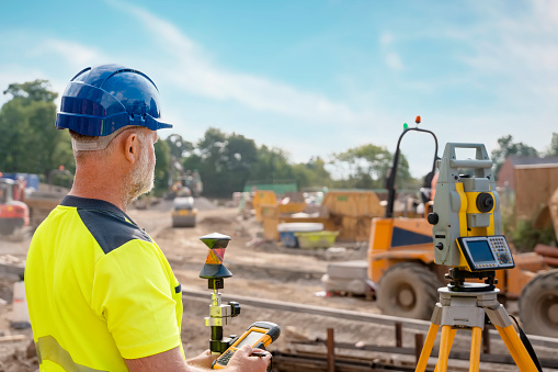 A man site engineer surveyor working with theodolite total station EDM equipment on a building construction site outdoors