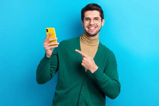 Photo of confident positive guy dressed green cardigan eyewear pointing apple samsung iphone modern gadget isolated blue color background.