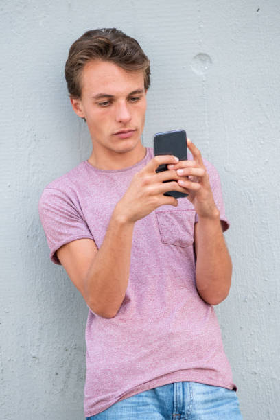 istock Young man leaning against wall and looking at cellphone 1644228102