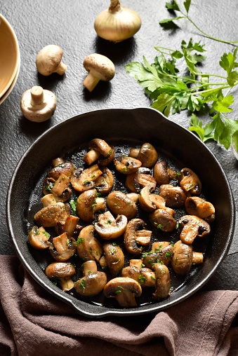 Roasted mushroom in cast iron pan over dark stone background. Vegetarian vegan food concept. Close up view