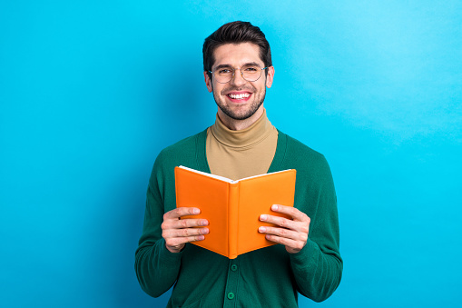 Photo of cheerful student young guy university wear green jumper beige turtleneck hold book reader isolated on blue color background.