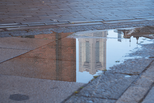 Depressed and loneliness mood concept. Blurry reflection in a rain puddle of alone walking person on wet city street during rainy weather.