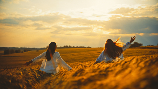 Carefree female friends amidst wheat crops in farm enjoying vacation together during sunset