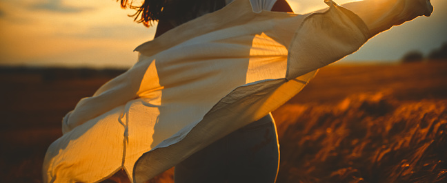 Midsection of carefree young woman running amidst wheat crops and enjoying sunset