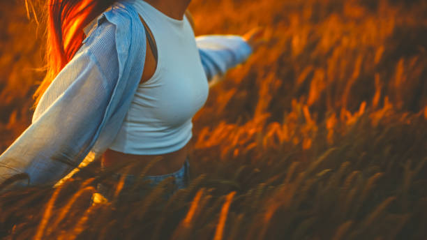 Midsection of young woman walking amidst crops in farm and enjoying sunset during vacation