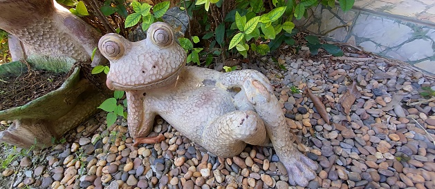 a photography of a frog statue sitting on a rock next to a potted plant.
