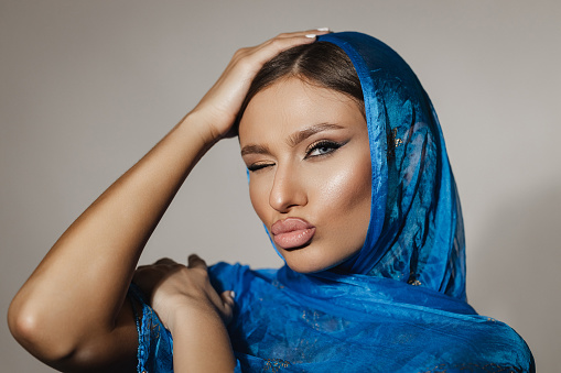 Portrait of a beautiful young woman wearing a blue color head scarf, studio shot in front of a white background