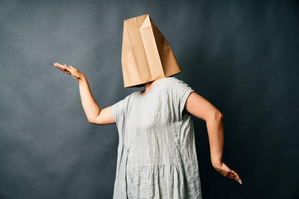 Woman with paper bag over her head dancing on dark background. stock photo