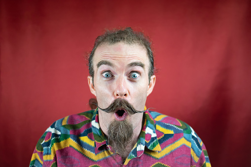 Hipster man with mustache, amazed, mouth open and shocked expression like Sales with red background