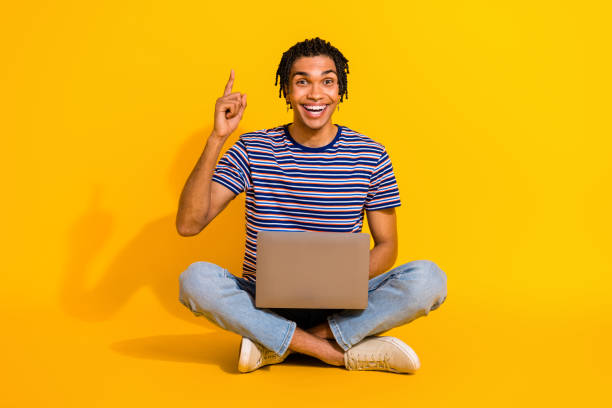 istock Full length portrait of overjoyed handsome guy sit floor use netbook point finger up empty space isolated on yellow color background 1644323276