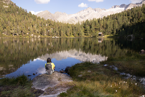 A man with a backpack sits on a rock on the shore of a beautiful alpine lake with a symmetrical reflection, Austria. High quality photo