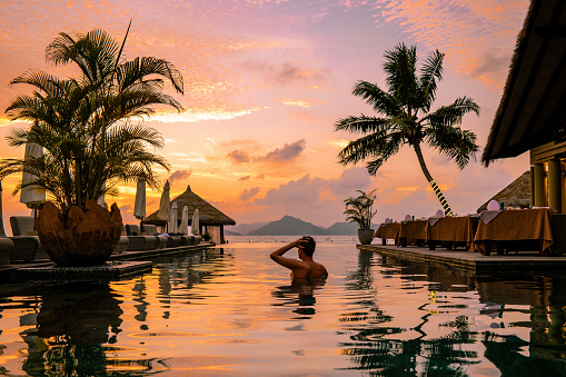 Luxury swimming pool in tropical resort, relaxing holidays in Seychelles islands. La Digue, Young man during sunset by swimpool Seychelles