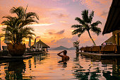 Luxury swimming pool in tropical resort, relaxing holidays in Seychelles islands. La Digue, Young man during sunset by swimpool