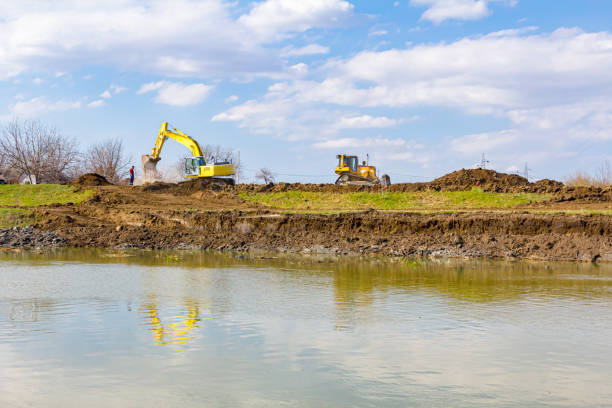Excavators and bulldozer are moving earth to level, equates river coast, project for bridge foundation is in progress.