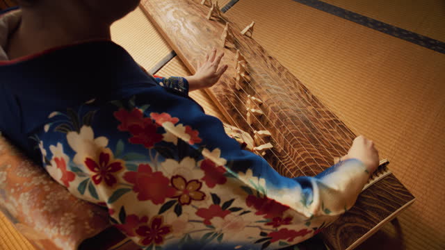 Over the Shoulder Footage of a Female Playing on a Japanese Koto. Woman Wearing a Blue Kimono with Colorful Flower Ornaments, Skilfully Using Her Hands on a Traditional String Instrument
