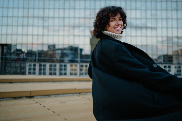 istock Smiling young woman looking over her shoulder while turning and her coat sways. 1644399432