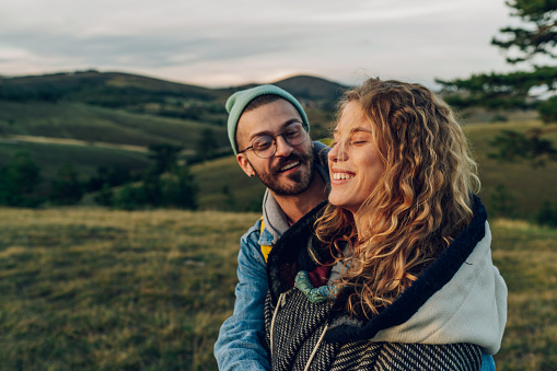 Happy couple in love embracing and following trail along grassy mountain ridge and having fun together while walking in the nature. Healthy lifestyle and romantic getaway. Focus on a smiling woman..