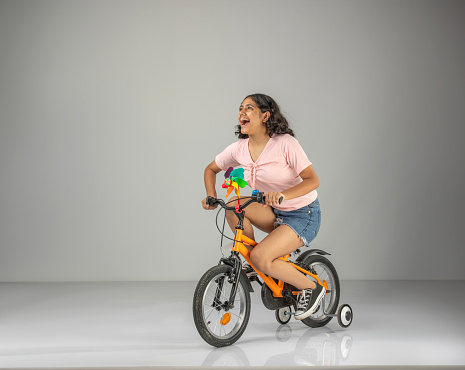 Carefree teenage girl looking away and laughing cheerfully while riding bicycle against white background