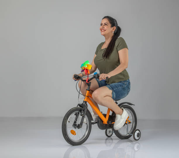 women with a sports figure in sports summer outfit victoriously holds a bicycle above her head and laughs against a dark background in blue and white streaks of smoke and dust. Athlete's victory.